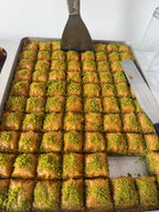 Baklava with green pistachios on a baking tray with a spatula.