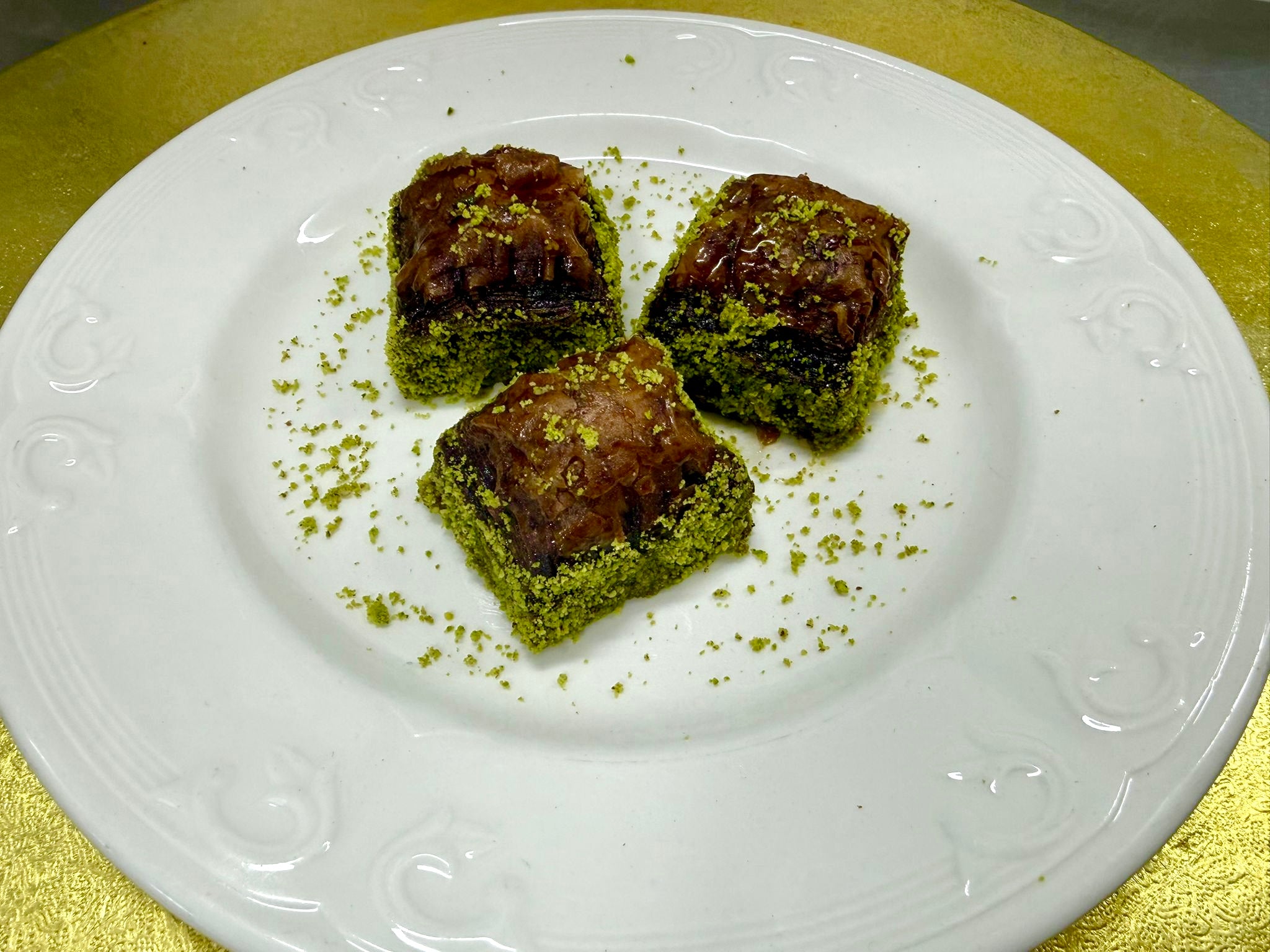 Three Chocolate baklava with green Antep pistachios on a white plate with a gold background
