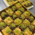 Two gold trays filled with green pistachio baklava on a gray surface.