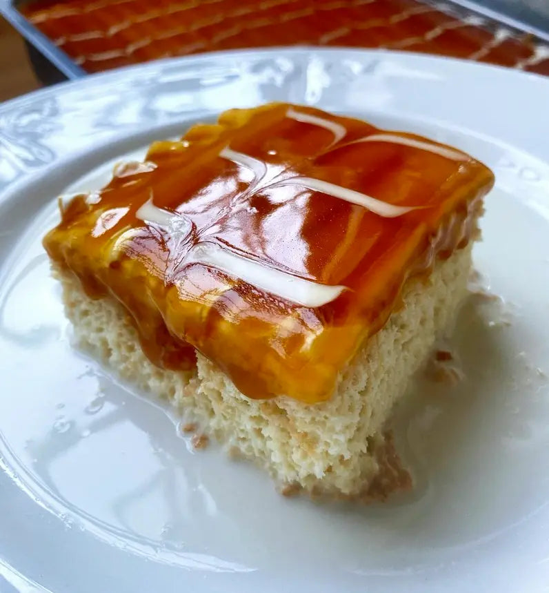 A slice of soft Trilece milk cake glazed with rich caramel sauce and white cream patterns.