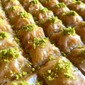 Rows of classic golden baklava squares, each topped with a vibrant mound of premium Antep pistachios.