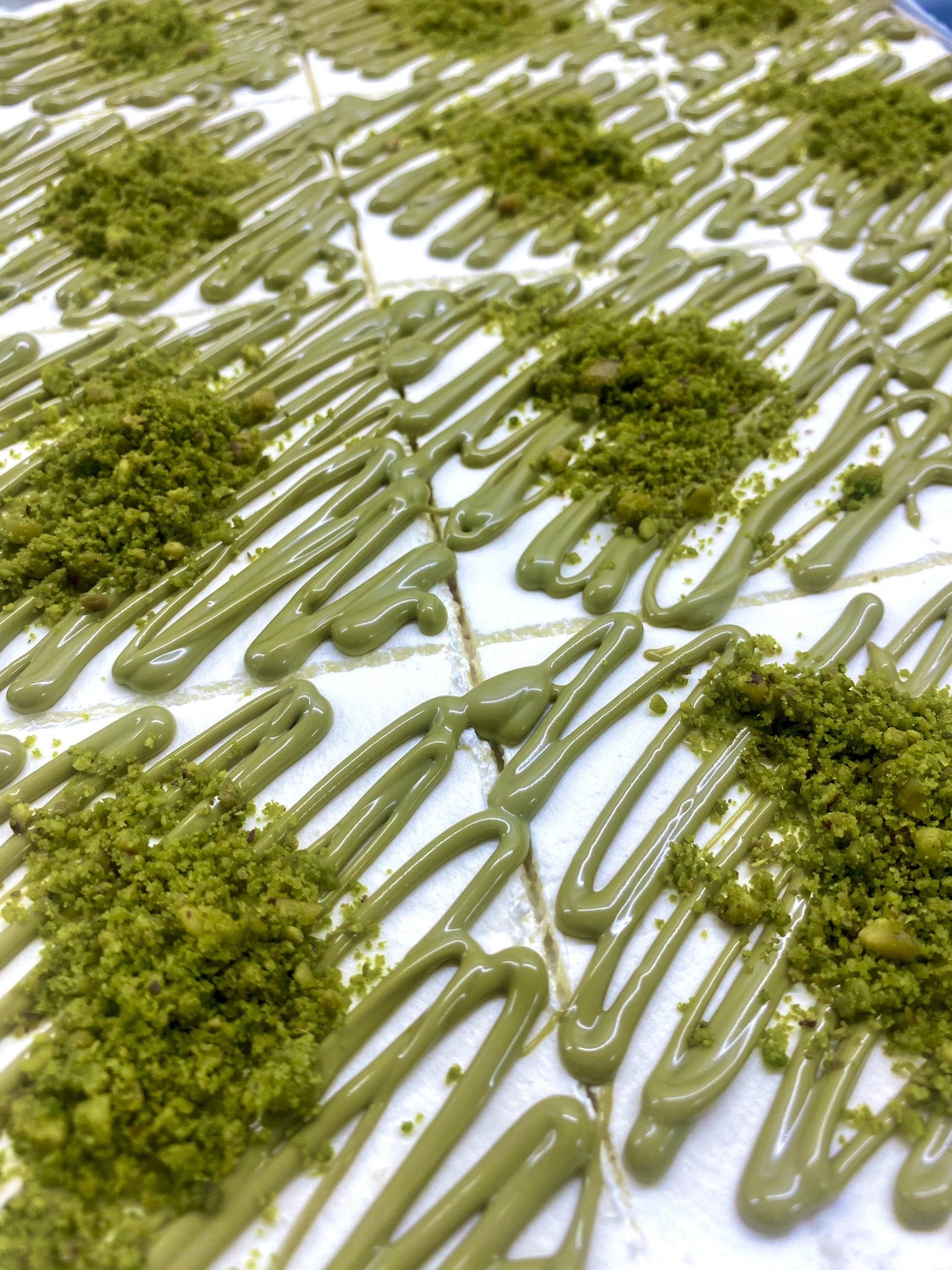 Trilece milk cake decorated with green pistachio sauce drizzle and crushed pistachio nuts.