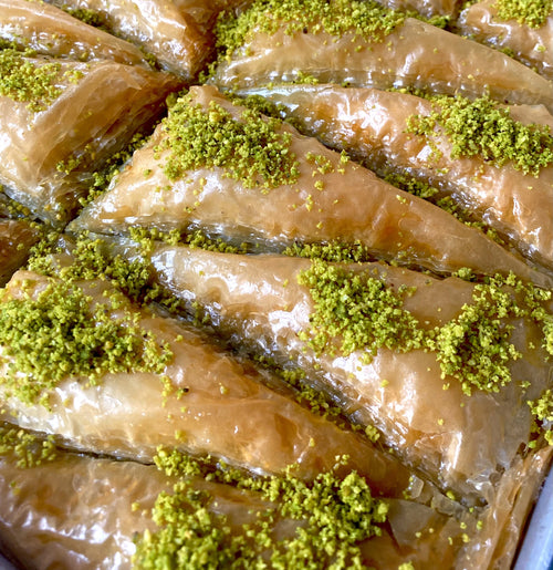 Layers of flaky triangle-shaped baklava filled and topped with green pistachios.
